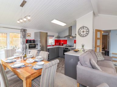 A kitchen and dining area with a wooden table set for six and a gray sofa at Limefitt Lodge Fellside 8 Limefitt Park near Windermere