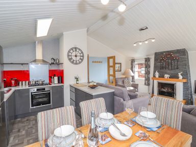 An open kitchen and living room with a dining table set for four and a fireplace at Limefitt Lodge Fellside 8 Limefitt Park near Windermere