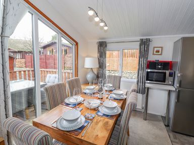 A dining area with a wooden table set for six people and striped chairs near large windows at Limefitt Lodge Fellside 8 Limefitt Park near Windermere
