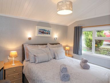 A bedroom with a bed with multiple pillows and rolled towels bedside tables with lamps and a window with gray curtains at Limefitt Lodge Fellside 8 Limefitt Park near Windermere