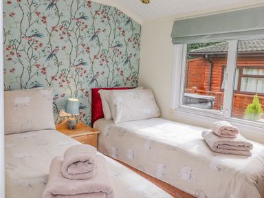 A bedroom with two single beds with sheep bedding a wooden nightstand and a window showing a wooden cabin outside at Limefitt Lodge Fellside 8 Limefitt Park near Windermere