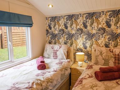 A bedroom with two single beds a nightstand with a lamp and a window with a blue blind at Limefitt Lodge Fellside 8 Limefitt Park near Windermere