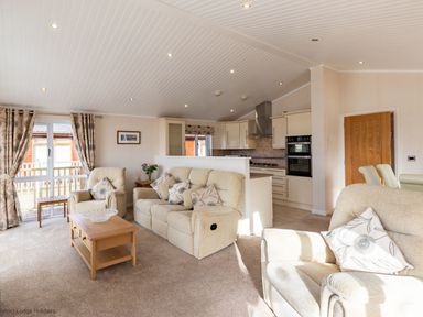 A living room with beige sofas and a wooden coffee table next to a kitchen with white cabinets at Waterbird in Lakeview 4 White Cross Bay near Windermere