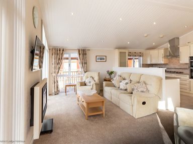 A living room with sofas coffee table wall-mounted TV and kitchen in the background at Waterbird Lakeview 4 White Cross Bay near Windermere