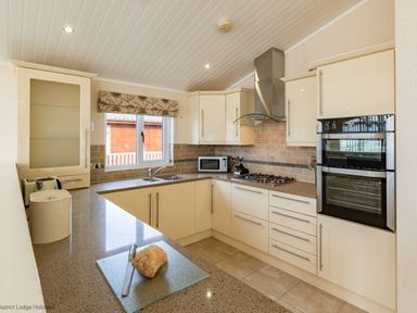 A kitchen with cream cabinets a gas stove built in ovens microwave and a loaf of bread on the counter at Waterbird Lakeview 4 White Cross Bay near Windermere