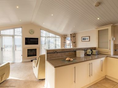 A kitchen with countertop appliances and a living area with chairs and a wall-mounted TV at Waterbird Lakeview 4 White Cross Bay near Windermere