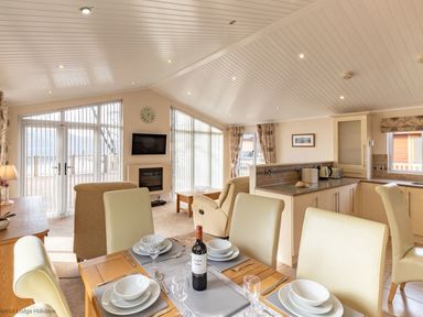 An open plan dining and living area with a set dining table a kitchen with cream cabinets and a sitting area with armchairs at Waterbird Lakeview 4 White Cross Bay near Windermere