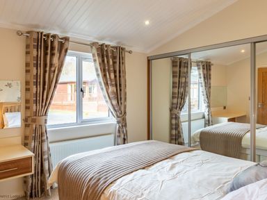 A bedroom with a bed near a window with curtains and a mirrored wardrobe at Waterbird Lakeview 4 White Cross Bay near Windermere
