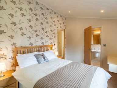 A bedroom with a double bed a nightstand with a lamp doors leading to a bathroom and hallway at Waterbird Lakeview 4 White Cross Bay near Windermere