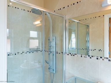 A shower area with glass doors and tiled walls with a decorative border at Waterbird Lakeview 4 White Cross Bay near Windermere