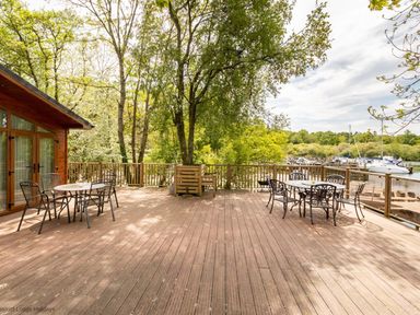 A wooden deck with two metal tables and chairs overlooking boats on water at Waterbird Lakeview 4 White Cross Bay near Windermere