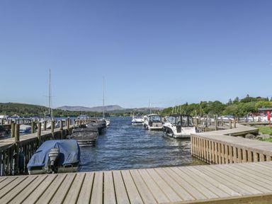 A wooden dock with boats moored on either side on a lake surrounded by trees and hills at Glenridding Lodge in Grasmere 2 White Cross Bay near Windermere