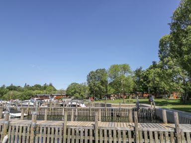 A wooden dock with boats and a grassy area with trees and benches at Glenridding Lodge in Grasmere 2 White Cross Bay near Windermere