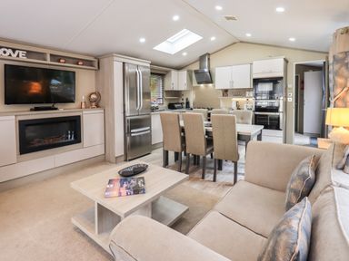 An open plan living room and kitchen with sofa, dining table with six chairs, refrigerator, and television at Glenridding Lodge in Grasmere 2 White Cross Bay near Windermere