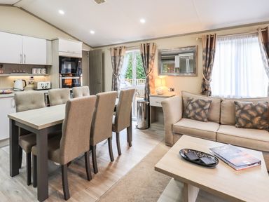 A dining area with a table and six chairs next to a kitchen and a living room with a sofa and coffee table at Glenridding Lodge Grasmere 2 White Cross Bay near Windermere