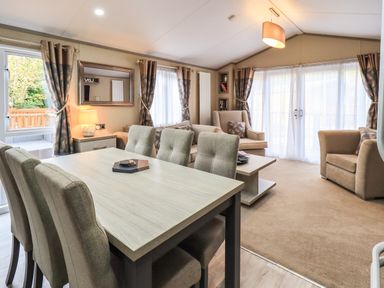 A living room and dining area with a table and chairs next to a seating area with armchairs and a sofa at Glenridding Lodge in Grasmere 2 White Cross Bay near Windermere