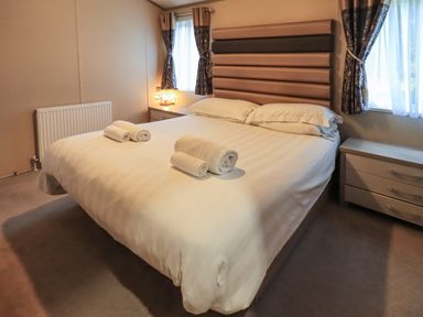 A bedroom with a bed with white bedding and rolled towels on it at Glenridding Lodge in Grasmere 2 White Cross Bay near Windermere