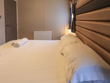 A bedroom with a bed with white sheets pillows and rolled towels a wooden door and a radiator at Glenridding Lodge Grasmere 2 White Cross Bay near Windermere