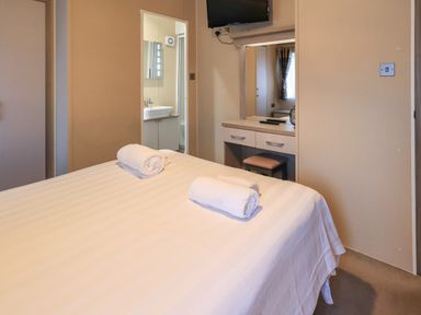 A bedroom with a bed and two rolled towels next to a dressing table and a bathroom door at Glenridding Lodge Grasmere 2 White Cross Bay near Windermere