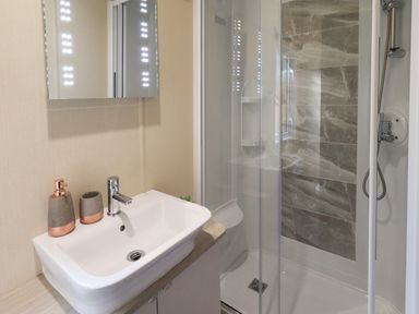 A bathroom with a white sink and faucet next to a glass-enclosed shower with tiled walls at Glenridding Lodge Grasmere 2 White Cross Bay near Windermere