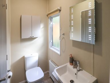 A bathroom with a toilet a sink a lighted mirror a window and a wall cabinet at Glenridding Lodge Grasmere 2 White Cross Bay near Windermere