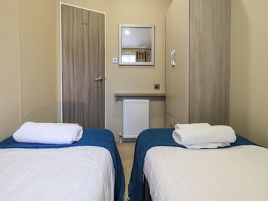 A bedroom with two single beds with towels on top a door a mirror and a wardrobe at Glenridding Lodge Grasmere 2 White Cross Bay near Windermere