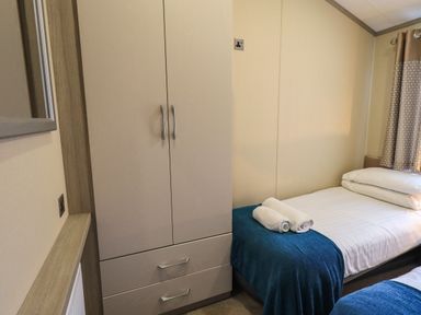 A bedroom with a wardrobe a bed with white linens blue blanket and rolled white towels at Glenridding Lodge Grasmere 2 White Cross Bay near Windermere