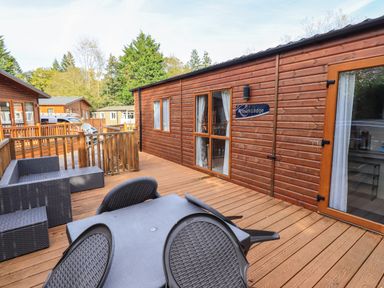 An outdoor wooden deck with black patio furniture and a wooden lodge named Artisan Lodge in Grasmere 2 White Cross Bay near Windermere