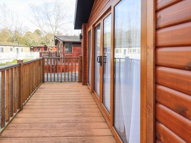 An outdoor wooden deck with railing and sliding glass doors at Glenridding Lodge in Grasmere 2 White Cross Bay near Windermere