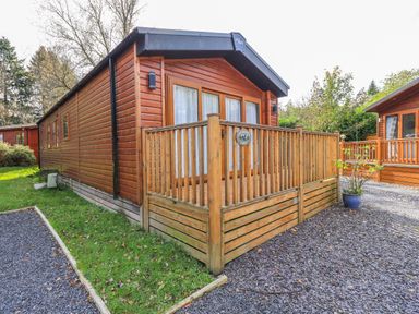 A wooden cabin with porch railing and gravel path at Glenridding Lodge in Grasmere 2 White Cross Bay near Windermere