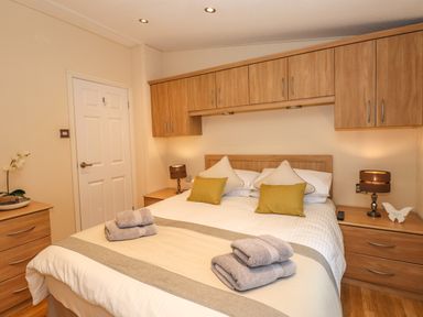 A bedroom with a double bed bedside tables with lamps and overhead wooden cabinets at Wainwright Lodge Kirkstone 27 Limefitt Park near Windermere