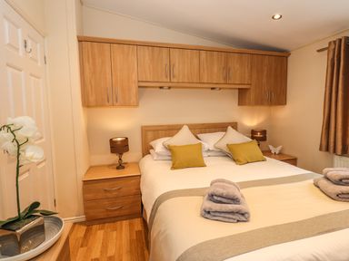 A bedroom with a bed, bedside tables, lamps, cabinets above the bed, and towels on the bed at Wainwright Lodge in Kirkstone 27 Limefitt Park near Windermere