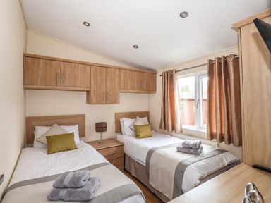 A bedroom with two single beds with towels on them a bedside table and wooden cabinets at Wainwright Lodge Kirkstone 27 Limefitt Park near Windermere
