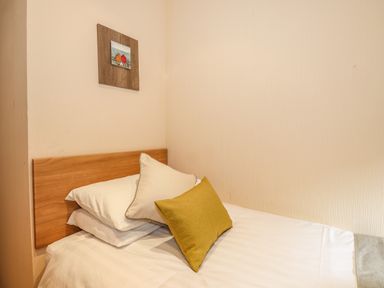 A bed with white pillows and a yellow cushion in a room with a wooden headboard and a painting on the wall at Wainwright Lodge Kirkstone 27 Limefitt Park near Windermere