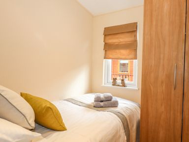 A small bedroom with a bed with pillows and folded towels near a window with a blind and a wooden wardrobe at Wainwright Lodge in Kirkstone 27 Limefitt Park near Windermere