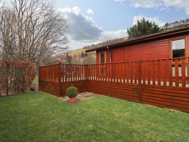 A wooden deck attached to a building with green grass and trees surrounding it at Wainwright Lodge Kirkstone 27 Limefitt Park near Windermere