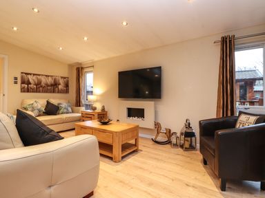 A living room with cream sofas dark armchair wooden coffee table and wall mounted TV at Wainwright Lodge Kirkstone 27 Limefitt Park near Windermere