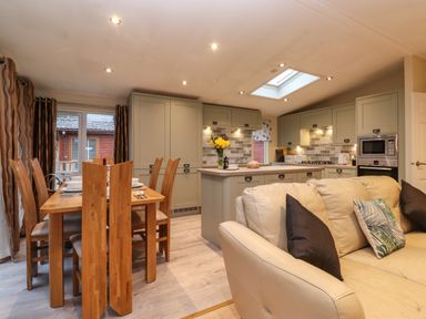 A kitchen and dining area with wooden dining table and chairs and cream sofa at Wainwright Lodge Kirkstone 27 Limefitt Park near Windermere