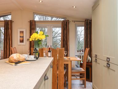 A dining area with wooden table and chairs a countertop with bread and coffee cups and windows with brown curtains at Wainwright Lodge Kirkstone 27 Limefitt Park near Windermere