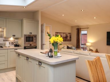 A kitchen island with flowers next to a living room with sofas and a lamp at Wainwright Lodge Kirkstone 27 Limefitt Park near Windermere