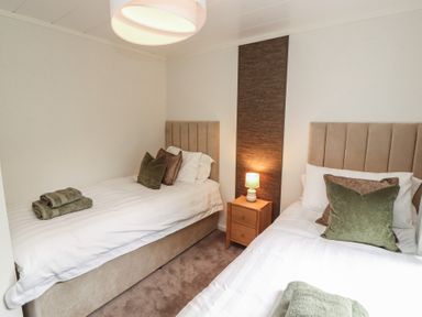 A bedroom with two beds and a bedside table at Beech Grove Lodge, Glade 17, Fallbarrow Park near Bowness on Windermere