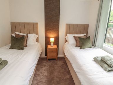 A bedroom with two single beds and a bedside table at Beech Grove Lodge, Glade 17, Fallbarrow Park near Bowness on Windermere