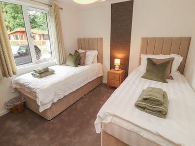 A bedroom with two single beds and a nightstand at Beech Grove Lodge, Glade 17, Fallbarrow Park near Bowness on Windermere