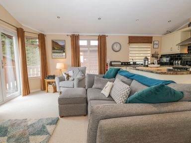 A living room with a grey couch and armchair next to a kitchen area at Pheasant's Nest Kirkstone 11 Limefitt Park near Windermere