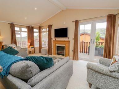 A living room with grey sofas a wall-mounted TV and large windows at Pheasant's Nest Kirkstone 11 Limefitt Park near Windermere