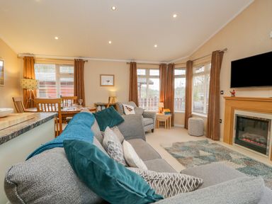 A living room with a grey sofa and teal cushions next to a fireplace and a dining area at Pheasant's Nest Kirkstone 11 Limefitt Park near Windermere