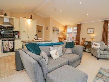 A living room with grey sofas and an open kitchen in the background at Pheasant's Nest Kirkstone 11 Limefitt Park near Windermere