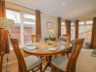A dining area with a wooden table set for four with wine glasses a bottle of wine and beige curtains at Pheasant's Nest Kirkstone 11 Limefitt Park near Windermere