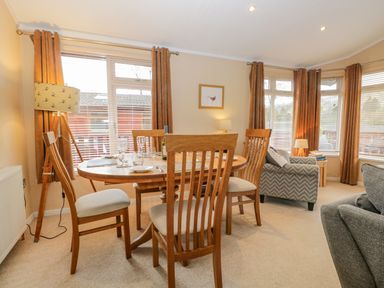 A dining room table with chairs and a lamp beside windows at Pheasant's Nest in Kirkstone 11 Limefitt Park near Windermere