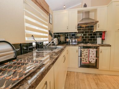 A kitchen with cream cabinets black tiled backsplash and brown countertop at Pheasant's Nest Kirkstone 11 Limefitt Park near Windermere